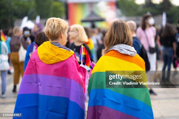 zwei frauen, die pride event sehen, eine trägt bisexuelle flagge und die andere pride-flagge - regenbogenfahne stock-fotos und bilder