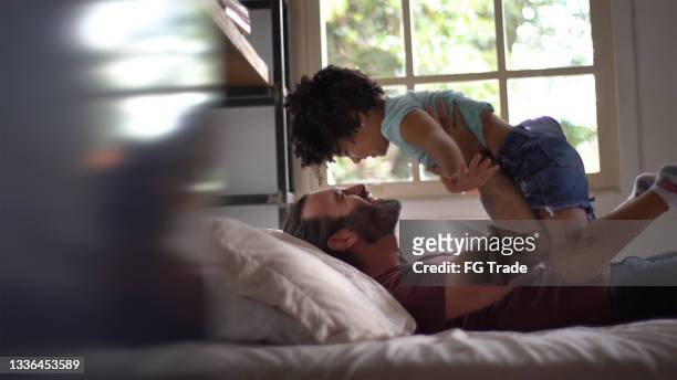 father playing with daughter lifting her up in the air in bed at home - dad throwing kid in air stockfoto's en -beelden