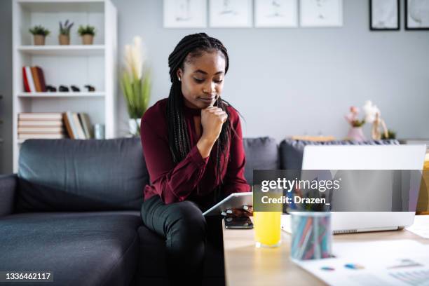 mujer africana seria que trabaja en casa, usando internet para aplicar en línea - búsqueda de trabajo fotografías e imágenes de stock