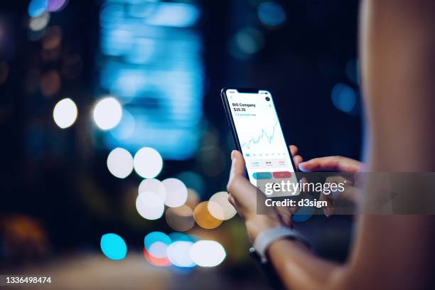 close up of businesswoman checking financial stock market analysis with mobile app on smartphone on the go, against illuminated corporate skyscrapers in financial district at night. financial investment, stock market and exchange, accounting concept - fintech stock-fotos und bilder