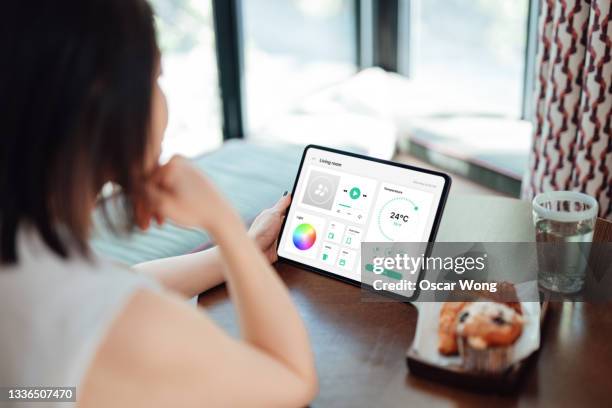 young woman using tablet to adjust the lighting equipment, control music, room temperature, oven, door lock, tv and kettle of a modern home - tablet screen home stock-fotos und bilder