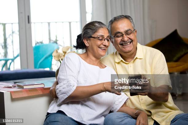 old couple enjoying using mobile phone at home - happy couple stock pictures, royalty-free photos & images