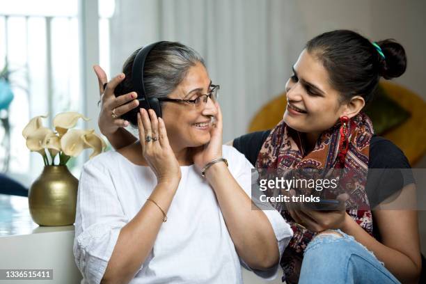 woman with senior mother listening music using headphones - mother in law stock pictures, royalty-free photos & images