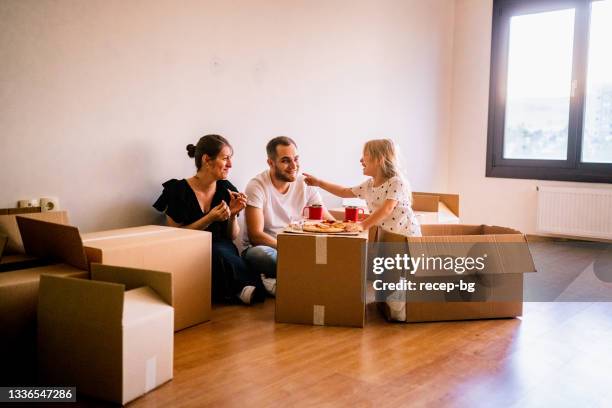 junge familie, die auf dem boden sitzt und im wohnzimmer ihres neuen hauses pizza essen - family photo in the delivery room stock-fotos und bilder