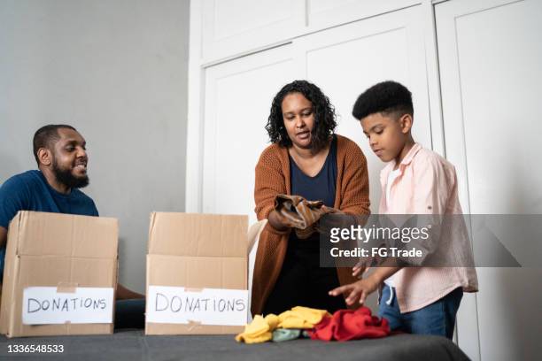parents with son sorting out clothes in boxes to donate at home - putting clothes son stock pictures, royalty-free photos & images