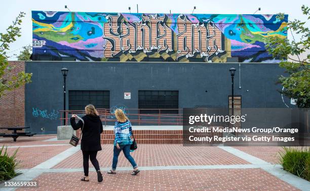 Two women walk past a colorful Santa Ana mural painted on the second floor of a building at the intersection of 4th and French Streets in downtown...
