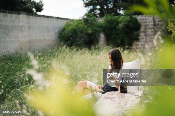 young woman relaxes with a book in a garden - coffee read stock pictures, royalty-free photos & images