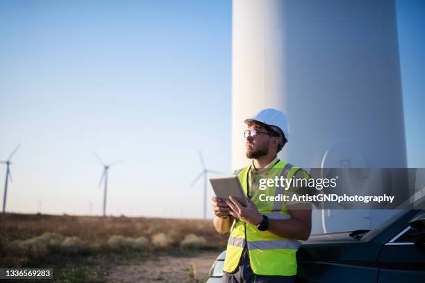 young engineer looking and checking wind turbines at field using digital tablet - wind farms stockfoto's en -beelden