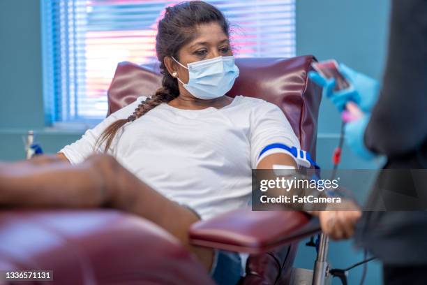 masked female adult donating blood at a clinic - blood bag 個照片及圖片檔