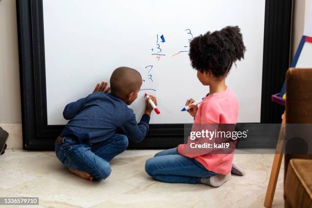 zwei afroamerikanische kinder rechnen auf whiteboard - mittleres kindesalter stock-fotos und bilder