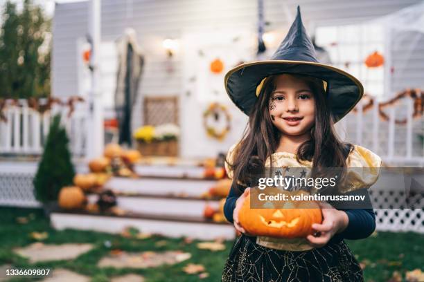 niña disfrazada de bruja sosteniendo jack-o-lantern pumpkins en halloween trick or treat - disfraces fotografías e imágenes de stock