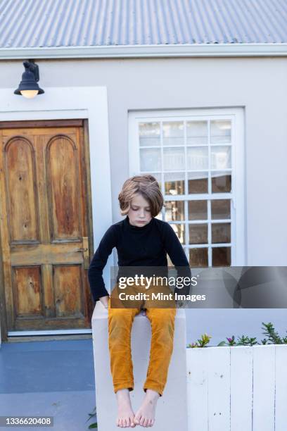 young boy sitting on a wall outside his home, waiting or bored - 70052 stock pictures, royalty-free photos & images