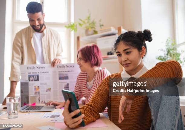group of young magazine editors indoors in office, using smartphone. - executive editor stockfoto's en -beelden