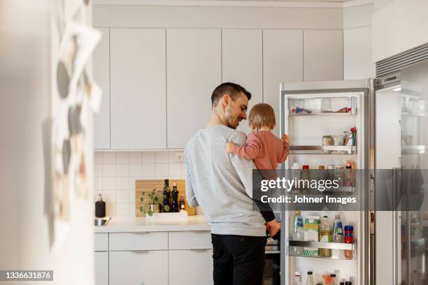 father carrying toddler daughter in kitchen - koelkast stockfoto's en -beelden