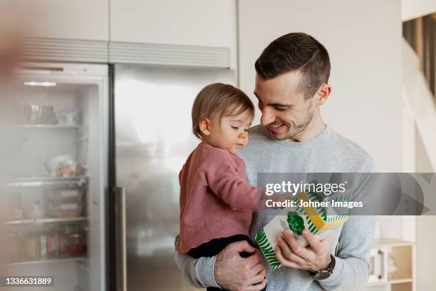 father carrying toddler daughter in kitchen - melkpak stockfoto's en -beelden