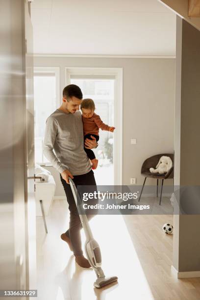 father carrying toddler daughter while vacuum cleaning - aspirapolvere foto e immagini stock
