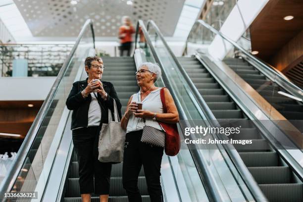 senior women standing on escalator - shopping centre escalator stock pictures, royalty-free photos & images