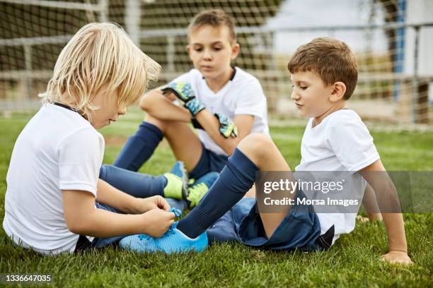 side view of girl helping boy tie shoe in soccer field - 釘鞋 個照片及圖片檔