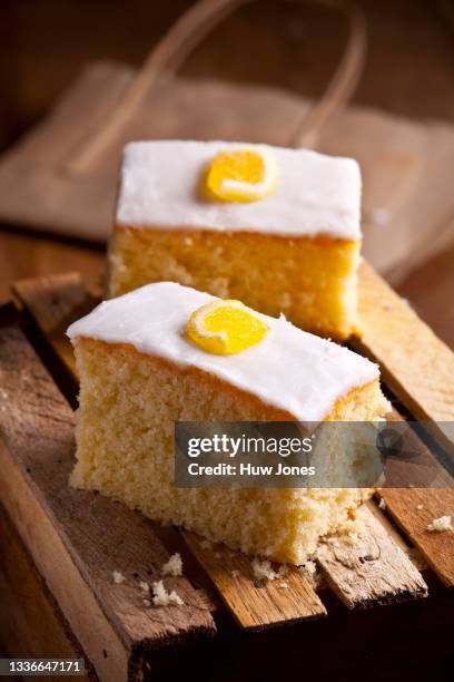 two slices of iced lemon cake on a wooden tabletop - zitronentorte stock-fotos und bilder