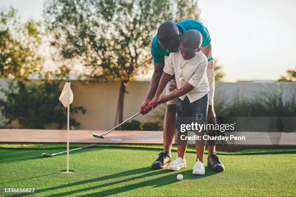 full length shot of a handsome young man and his son playing golf in their backyard - young men golfing stock pictures, royalty-free photos & images