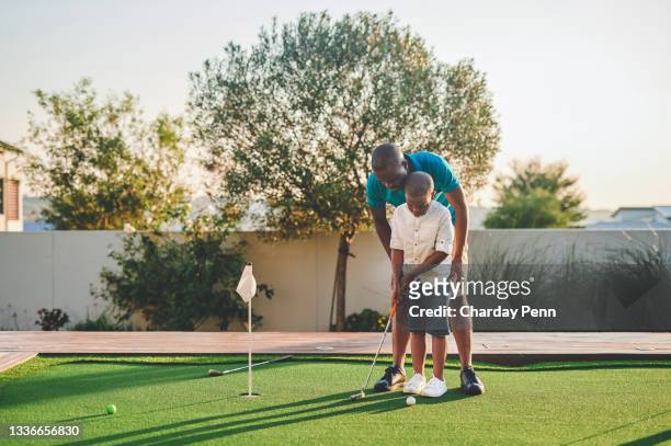 full length shot of a handsome young man and his son playing golf in their backyard - father son golf stock pictures, royalty-free photos & images