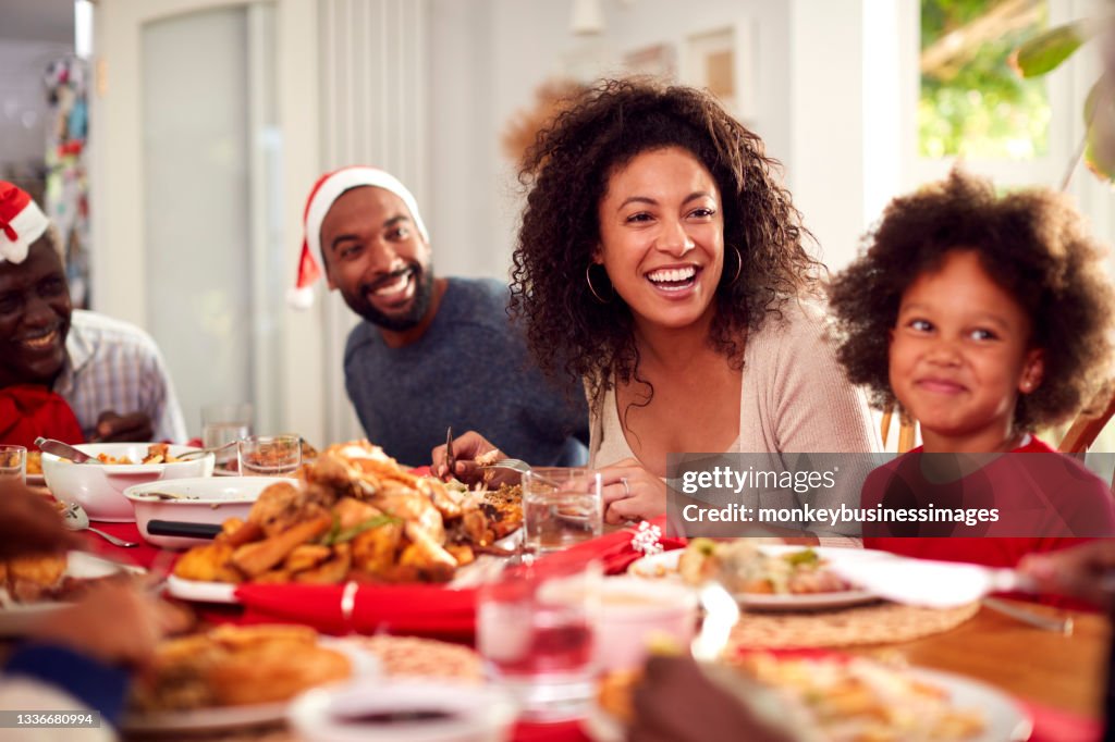 Multi Generation Family In Paper Hats Enjoying Eating Christmas Meal At Home Together