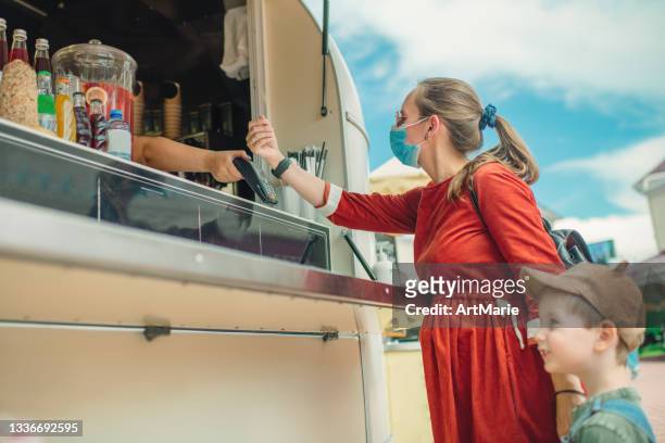 pregnant woman in protective face mask and her son buying food and drinks at food truck - smartwatch pay stock pictures, royalty-free photos & images
