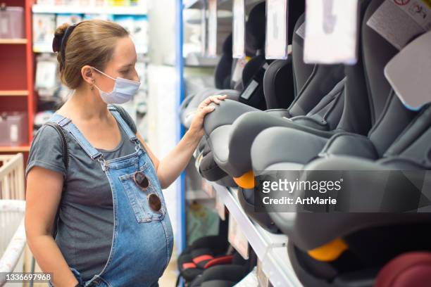 pregnant woman in protective face mask choosing car seat in a store - pregnant woman car stock pictures, royalty-free photos & images