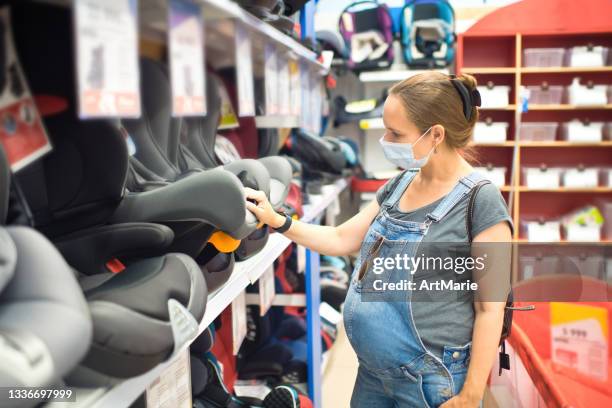 pregnant woman in protective face mask choosing car seat in a store - pregnant woman car stock pictures, royalty-free photos & images