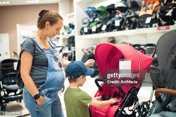 pregnant woman and her son choosing baby carriage in a store - kinderwagen stockfoto's en -beelden