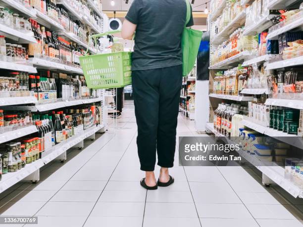 low section rear view cropped shot asian chinese mid adult woman shopping in supermarket carrying shopping basket and recycle bag in the aisle for daily necessities - shopping basket stock pictures, royalty-free photos & images