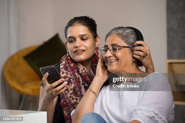 woman with senior mother listening music using headphones - indian mother daughter stock pictures, royalty-free photos & images
