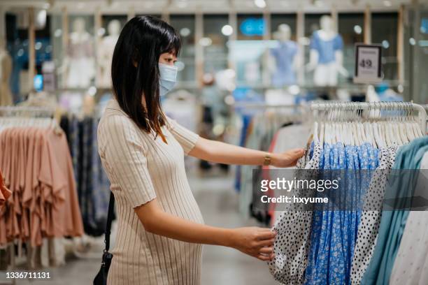 asian pregnant woman shopping in clothing store - maternity wear stock pictures, royalty-free photos & images