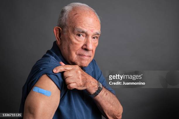 senior man posing showing his vaccination band-aid in his arm - man studio shot stock pictures, royalty-free photos & images