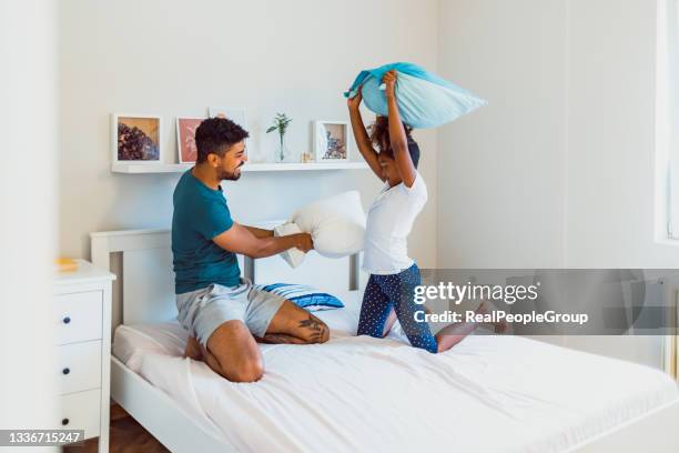 cute little girl and her father are fighting with pillows and smiling while sitting on bed at home - avoiding conflict stock pictures, royalty-free photos & images