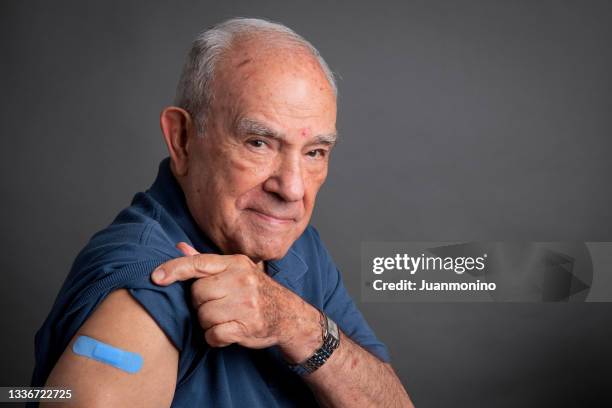 älterer mann posiert mit seinem impfpflaster im arm - old arm stock-fotos und bilder