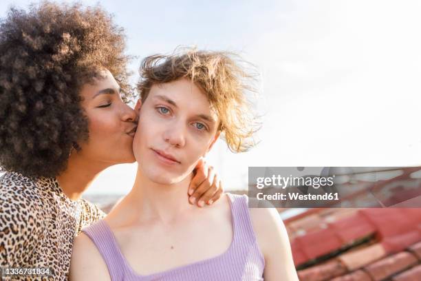 afro woman kissing male friend on building terrace - city photos stock-fotos und bilder