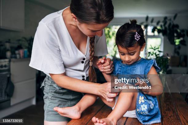 mother holding hand while putting bandage on daughter's knee at home - adhesive bandage stock pictures, royalty-free photos & images