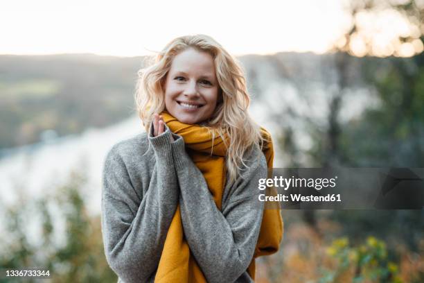 blond woman in gray sweater smiling during sunset - shawl stock-fotos und bilder