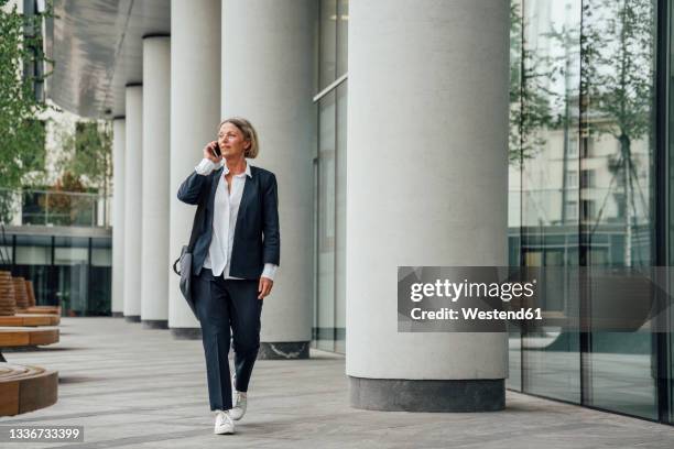 female professional talking on mobile phone while walking in office park - woman walking full length stock pictures, royalty-free photos & images