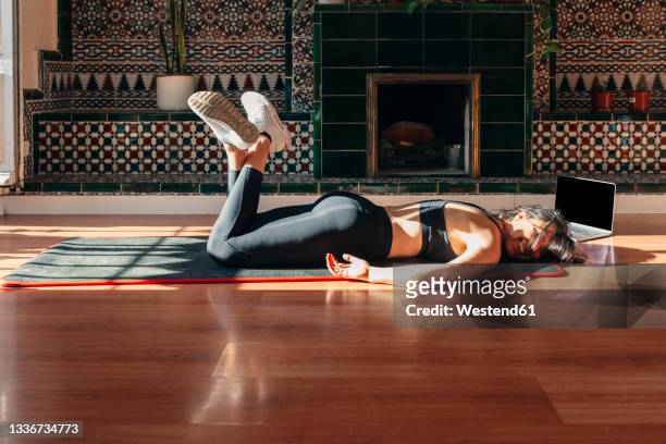 tired young woman lying on exercise mat during home workout - china foto e immagini stock