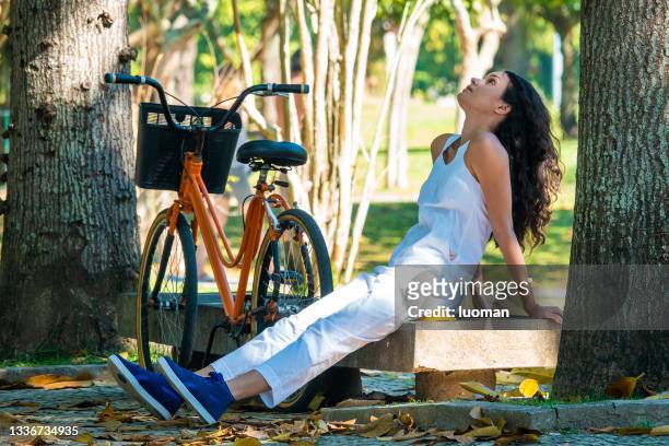 young woman sitting in the park beside the bicycle - jumpsuit 個照片及圖片檔