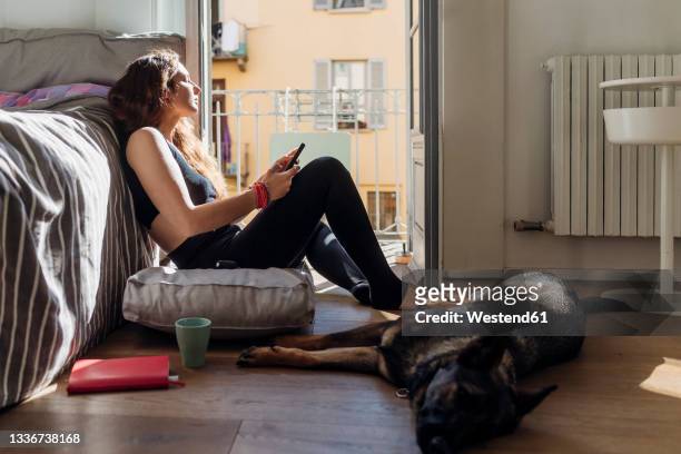 woman holding mobile phone while sitting with dog in bedroom - german shepherd sitting stock pictures, royalty-free photos & images