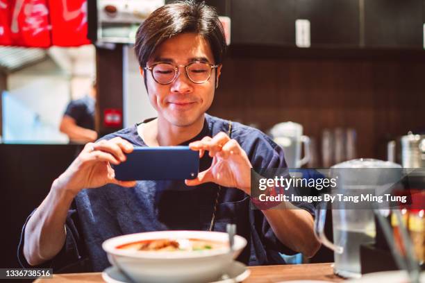 young cheerful man taking photo of freshly served japanese ramen with smartphone in a japanese restaurant - asian cuisine japanese cuisine stock pictures, royalty-free photos & images