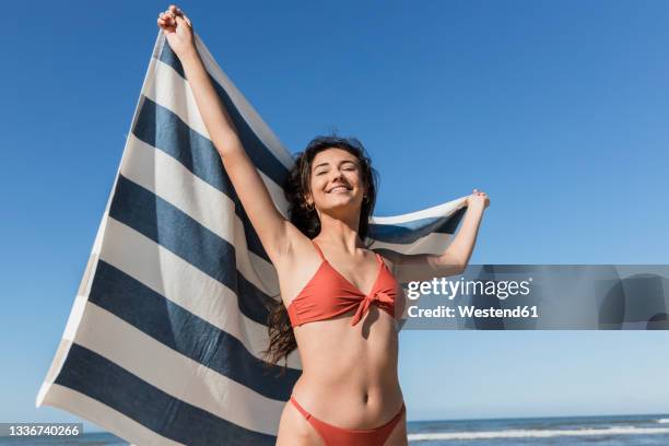 smiling woman with eyes closed holding towel at beach - woman towel beach stockfoto's en -beelden