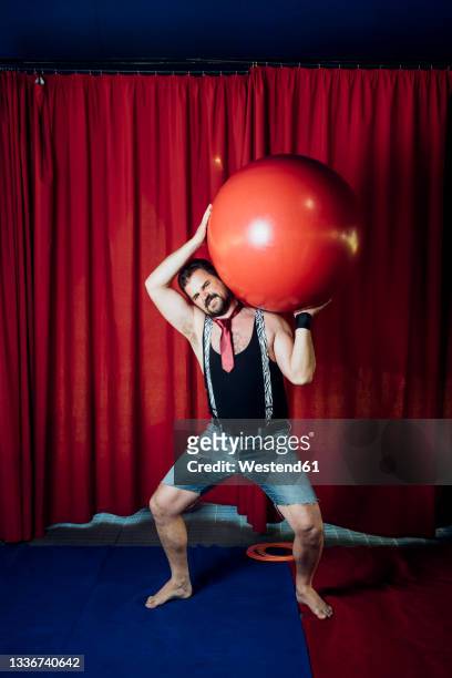 male circus acrobat carrying red ball while performing on stage - male gymnast photos et images de collection