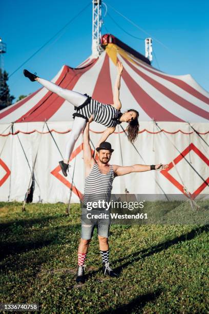 muscular male acrobat lifting female performer while standing on meadow - zirkuskünstler stock-fotos und bilder