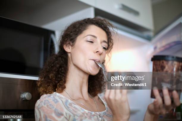 young woman eating ice cream in kitchen - lick foto e immagini stock