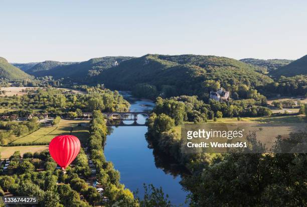 red hot air balloon flying over dordogne river - périgord photos et images de collection