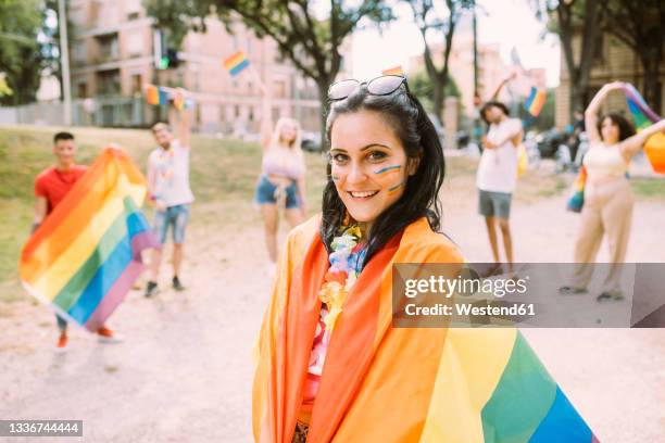 smiling woman wrapped in rainbow flag at park - gay flag stockfoto's en -beelden